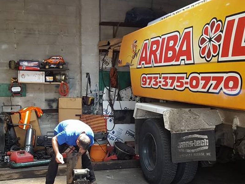 A mechanic servicing a yellow Ariba Oil truck inside the company shop.