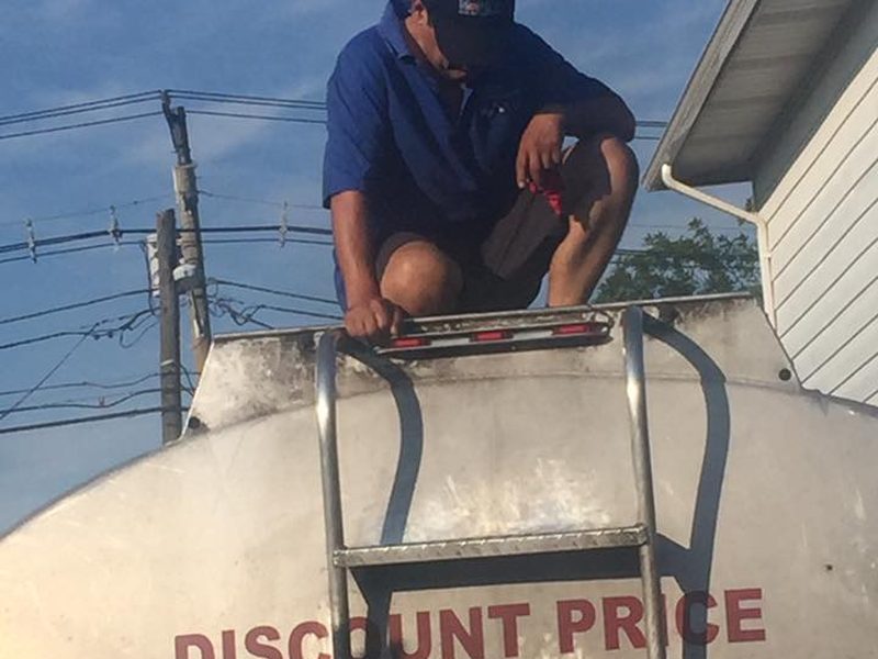 An Ariba Oil driver on top of a tanker truck marked discount price.
